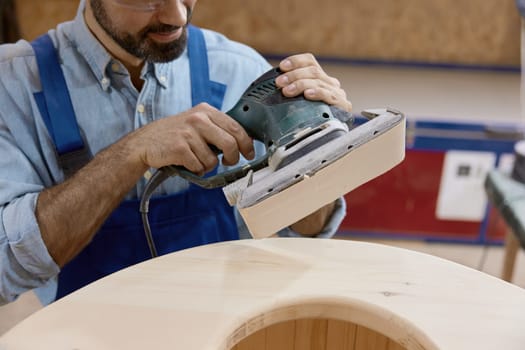 Woodworker using grinding machine for finishing wood construction. Timber surface polishing, renovation and restoration process with professional woodwork tools