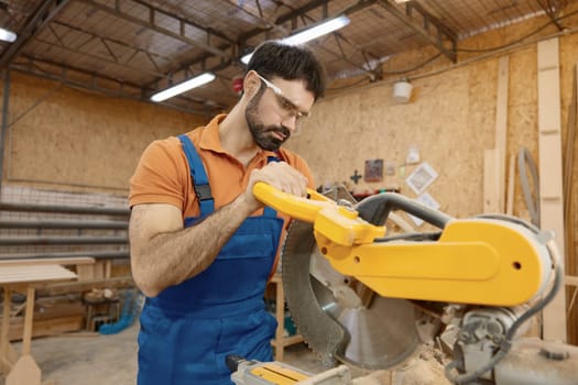 Male carpenter working with circular saw enjoying craftsmanship at workshop. Professional equipment for woodwork master for wooden furniture manufacturing