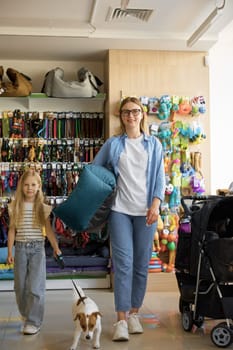 Full-length portrait of satisfied mother and daughter with dog at pet store. Cheerful parent and child shopping new soft comfortable doggy place for sleeping