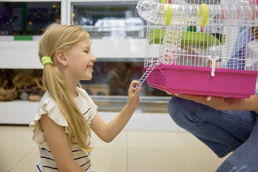 Cute daughter looking at new hamster cage in mother hands. Happy family shopping at pet store