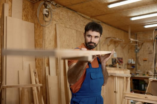 Portrait of artisan holding wooden timber checking plank straightness standing over woodwork studio background