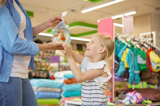 Happy satisfied mother and girl child holding new gold fish in plastic packet with water kneeling over pet shop background