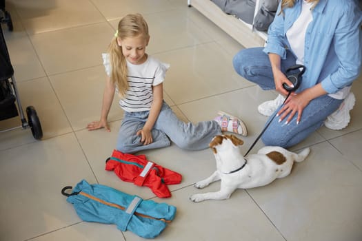 Portrait of little girl showing new comfort winter clothes for dog during shopping with mother at pet store