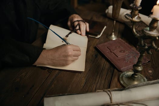 Crop shot of medieval monk chronicler writing ancient sacred manuscript under candlelight in dark monastery cell