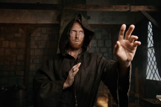 Portrait of friar wearing robe and golden cross reaching hand to camera. Monk demonstrating acceptance, forgiveness and attracting to faith