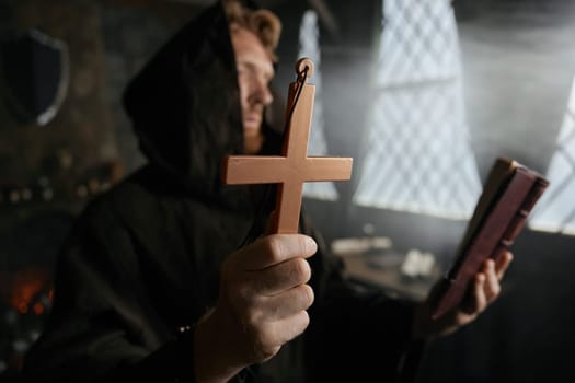 Priest holding cross and holy bible reading prayer and performing exorcism rite selective focus