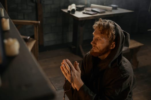 Desperate priest with folded praying hands kneeling before church altar in mystical smoke