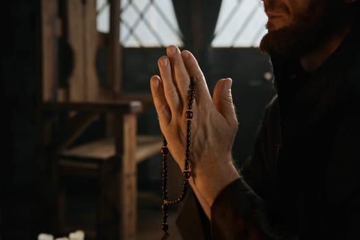 Monk folded hands in praying position with rosary beads closeup. Prayer repetition, faith and worship concept