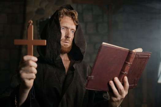 Priest holding cross and holy bible reading prayer and performing exorcism rite selective focus