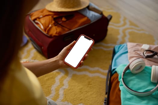 Empty blank screen on mobile phone in female traveler hand over opened luggage suitcase folded for vacation