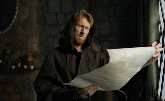 Medieval monk reading obsolete historical parchments and holy manuscripts. Abbey chronicler preparing monastic archive