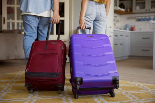 Crop view of couple leaving home apartment with packed luggage ready for summer vacation trip, young man and woman feeling excitement and fun walking with suitcases