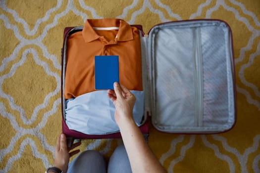 Closeup cropped shot of male hand holding paper passport document over folded clothes in travel suitcase. Preparation for vacation concept