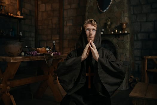 Desperate monk wearing robe wishing and praying to God looking upward in mediaeval monastery