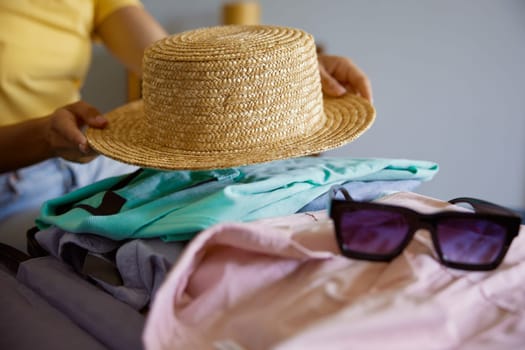 Unrecognizable woman traveler packing luggage preparing for summer vacation. Closeup view from above on female hands putting clothes and personal belongings into suitcase