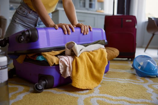 Cute woman trying to close overloaded travel bag during vacation preparation on summer weekends