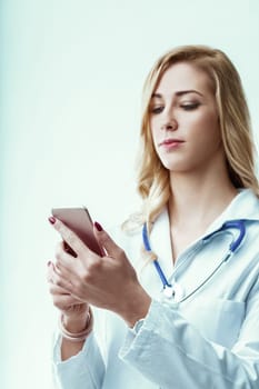 Young female doctor wearing a lab coat and stethoscope is engaged in reading medical news on her smartphone while navigating the fast-paced environment of the hospital