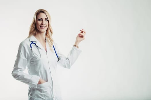 Young female doctor wearing lab coat and stethoscope smiling and gesturing with hand on white background, looking confident and professional