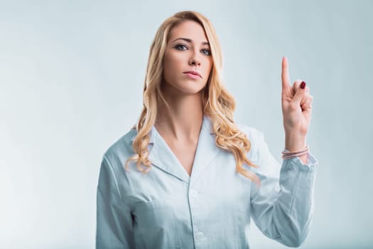 Young female doctor wearing a lab coat points her finger towards a transparent digital interface, showcasing the integration of artificial intelligence in healthcare