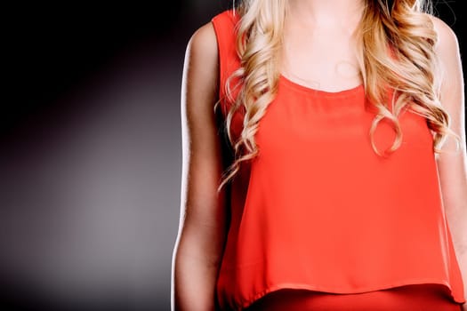 Close-up of a blond woman with curly hair, wearing a stylish red top, exuding confidence and elegance against a dark background, creating a visually striking image