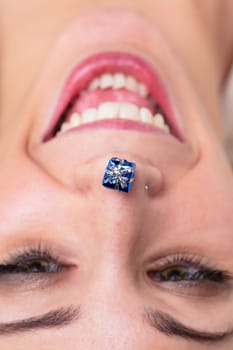 Close-up portrait of enthusiastic woman, upside-down head, mini-gift on her nose tip. Concept of gifts, holidays, celebrations