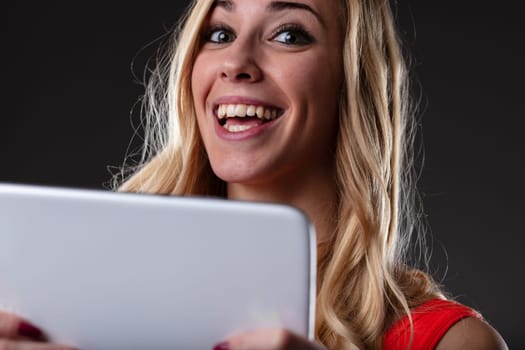 Happy young woman with a tablet excited about something online, be it a new series, shopping or great news. Dark contrasting background