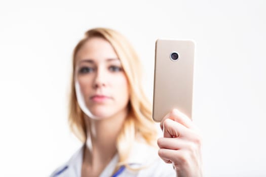 In-focus smartphone, held by a blurry blonde medic, highlights the utility of telemedicine and healthcare mobile apps