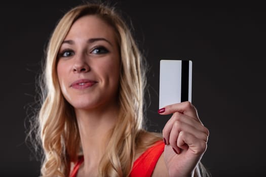 Excited woman with credit card ready for online shopping. Digital payments for convenience and speed. Blonde in orange, black backdrop, white card