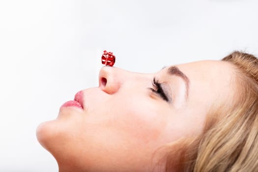 Side view of young woman, surprised and smiling, with mini gift on nose. Theme of gifting, Christmas, festivities  on white backdrop