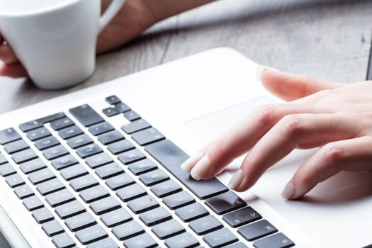 Businesswoman using the space bar on a laptop computer while enjoying a cup of hot beverage, close up focus of her hand and fingers