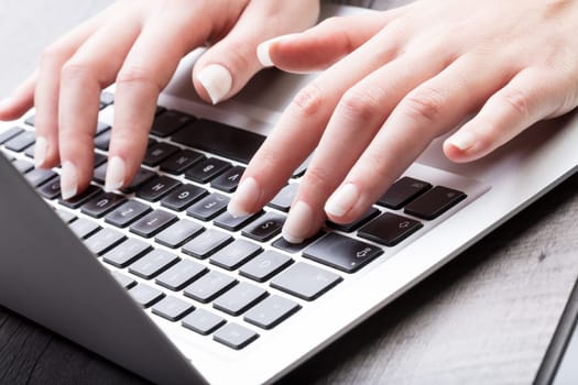 Young woman entering data on a laptop computer typing in the information, close up view of her hands in a study, communication or business concept