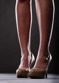 Legs in mid-high heels, closely shot, exuding sexiness and order. Lower legs of a fit woman, shaved and ending in mid-high animal print heels. Elegant dark background