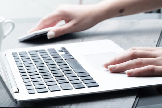 Businesswoman reaching for her mobile phone as she works on a laptop computer, low angle view of her hands