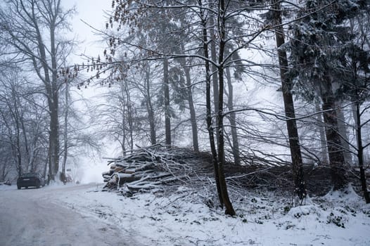 Winter landscape in a forest with lots of snow, snow-covered pile of wood, a road and a parked car