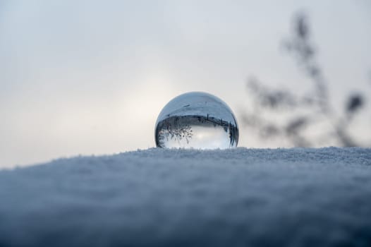 Glass ball lying in the snow on a cold winter day, with reflections of snow-covered landscape in the glass
