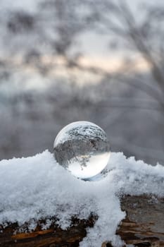 Glass ball lying in the snow on a cold winter day, with reflections of snow-covered landscape in the glass