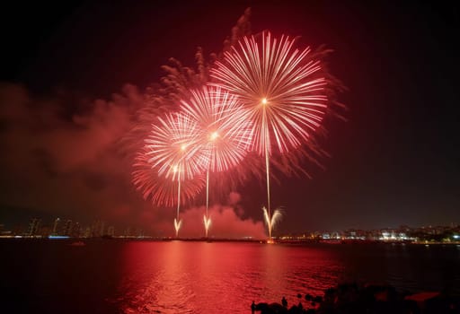 Brilliant red and gold fireworks explode against the dark sky, reflecting in the waterway. The celebration lights up the city skyline during a festive nighttime event. Generative AI.