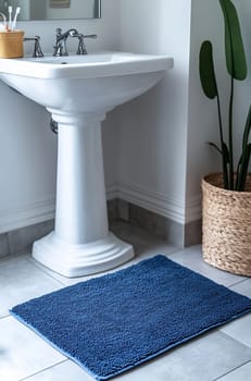A modern bathroom features a white sink beside a blue textured rug and a decorative plant in a woven basket, creating a serene atmosphere.