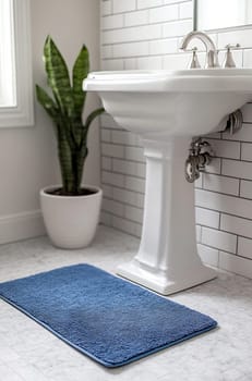 A stylish bathroom features a blue mat, a white pedestal sink, and a decorative plant beside it, creating a fresh and clean atmosphere.