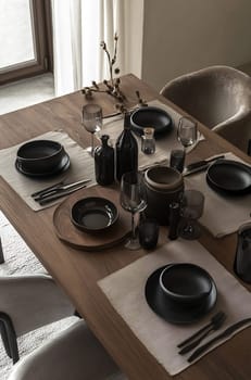 A beautifully arranged dining table features black plates, glassware, and neutral-colored placemats, creating a serene atmosphere.