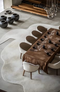 A long, stylish dining table is set with minimalistic tableware in a contemporary room featuring earthy tones and unique decor.
