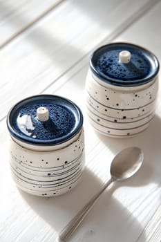 Two stylish ceramic containers sit on a wooden table, showcasing a modern design with blue and white accents. A silver spoon rests nearby.
