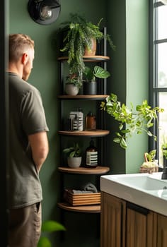 A man stands beside wooden shelves displaying various plants and bathroom products in a stylish green bathroom.