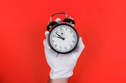 A white-gloved hand holds a classic black alarm clock against a bold red background, highlighting time management and punctuality. Near ten o clock