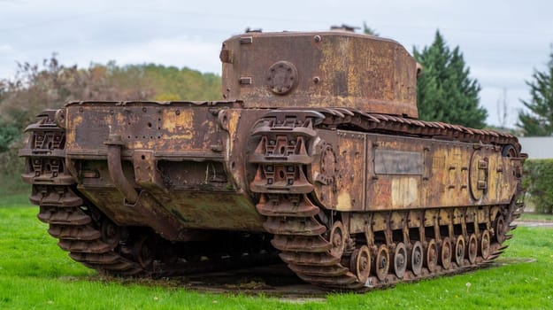 A rusted old tank is sitting in a grassy field. The tank is old and has a lot of rust on it. The tank is surrounded by trees and bushes, giving it a somewhat isolated and abandoned appearance