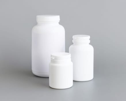 White plastic pill or capules bottles closeup against grey background. Packaging mockup for your pills or capsules, herbal supplement for helthcare