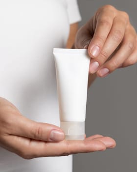 Close up of woman in white t-shirt holding blank squeeze cream tube close up, cosmetic mockup, copy space. Skincare beauty product. Female hands with natural nails