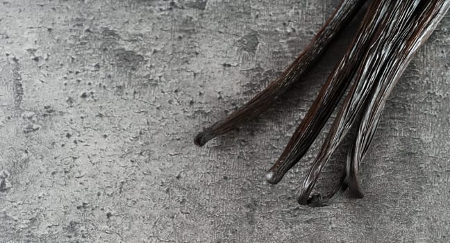 Four dark brown bourbon vanilla sticks on gray stone like board, empty space for text left side