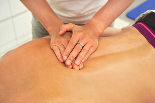 Female physiotherapist massaging muscles on back of her client lying at table, detail to her hands