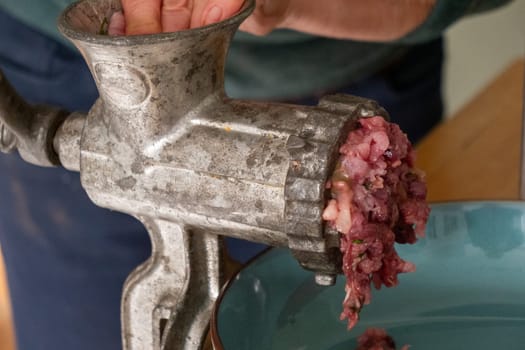 A person is using a meat grinder to grind meat. The meat is being ground into small pieces